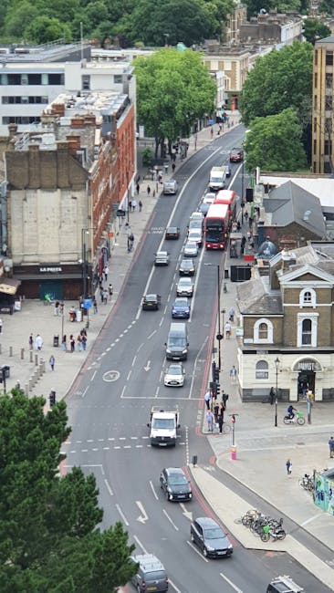 A street view capturing a narrow city road with a sloped incline, surrounded by multi-storey residential buildings made of brick and concrete. The road features a 'SLOW' road marking in white paint, w